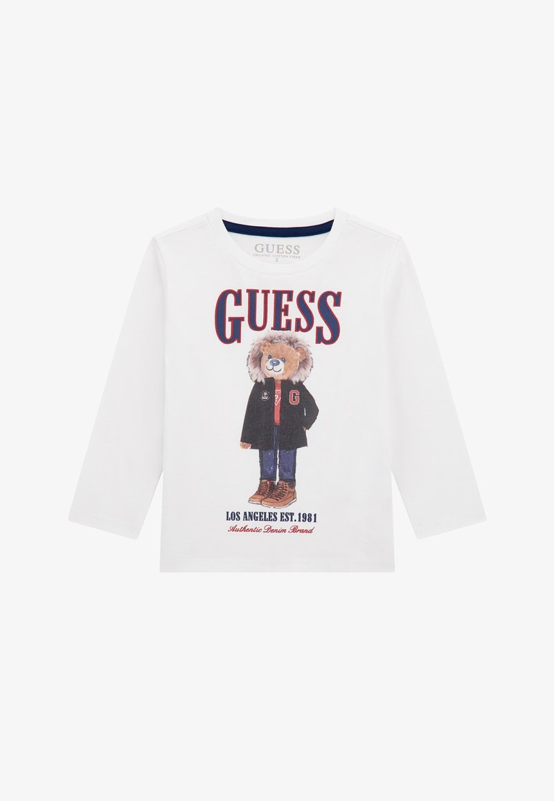 Langärmliges weißes T-Shirt aus Bio-Baumwolle mit einem Bärenmotiv in einer Jacke und braunen Stiefeln. Der Text beinhaltet "GUESS" und "LOS ANGELES EST. 1981."