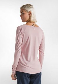 Langärmliges Oberteil aus weichem pinkfarbigen Stoff, mit weitem Ausschnitt, Raglanärmeln und einem kleinen Etikett auf der Rückseite. Glatte Textur und lockere Passform.