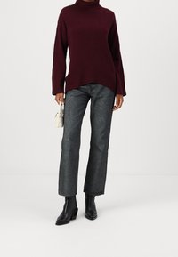 Burgundy polo-tröja, avslappnad passform, med långa ärmar. Strukturera grå raka byxor och svarta ankelstövlar. Minimalistisk vit handväska.