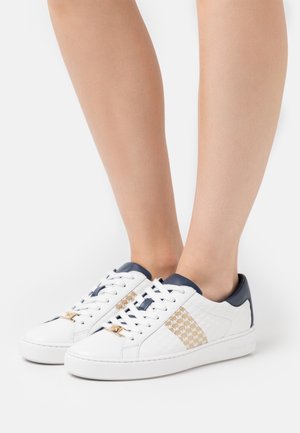 Valkoiset nahkakengät, joissa on teksturoitu sivupaneeli, laivastonsinisiä yksityiskohtia ja kultaiset logo-osat. Kengissä on klassinen nauhakiinnitys ja pyöreä kärki.