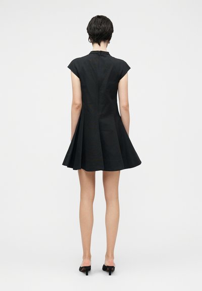 Juoda suknelė su trumpomis kepurėlės rankovėmis, prigludusiu liemeniu ir platėjančia sijonu. Medžiaga atrodo lygi, gale užsegama užtrauktuku.