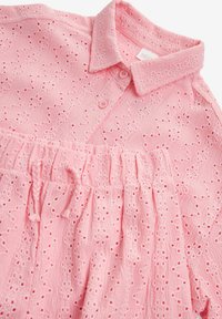 Ljust rosa blus med krage, knappstängning och broderat ögonhålsmönster. Texturerad tyg med samlad detalj vid midjan.