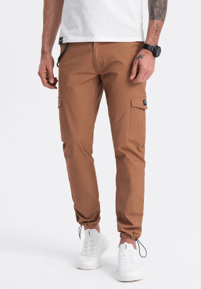Bruine cargobroek met elastische boorden, dikke stof, zijzakken en een afneembare trekkoord. Geharmoniseerd met witte sneakers.