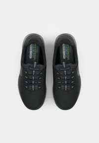 Melnas sporta kurpes ar tekstūras auduma augšdaļu, elastīgām auklām un mīkstinātu pēdu daļu ar uzrakstu "Atmiņas putas". Elegants dizains ar minimāliem akcentiem.