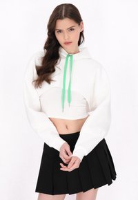 Biała krótka bluza z kapturem z zielonym sznurkiem i plisowaną czarną spódnicą. Bluza ma prosty krój i szerokie rękawy.