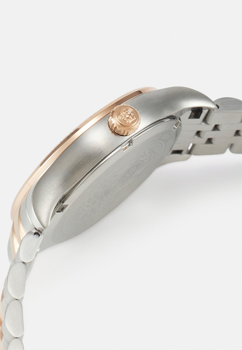 Reloj de pulsera de metal plateado y oro rosa con caja redonda, corona texturizada y correa enlazada, que presenta un diseño minimalista.