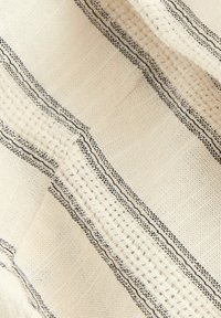 Tekstil med en cremet bundfarve og markante sorte striber samt vævede detaljer. Teksturen er blød og lidt grov med et lagdelt design.