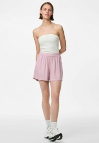 Shorts roses clairs avec une taille élastique, deux poches latérales et une coupe décontractée, associés à un haut blanc sans bretelles et des baskets blanches.