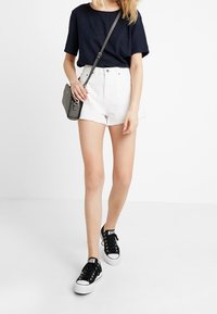 Bílé džíny kraťasy s roztrhanými okraji, doplněné námořnickou modrou blůzou s krátkým rukávem. Černé plátěné tenisky a malá šedá přes rameno taška dotvářejí vzhled.