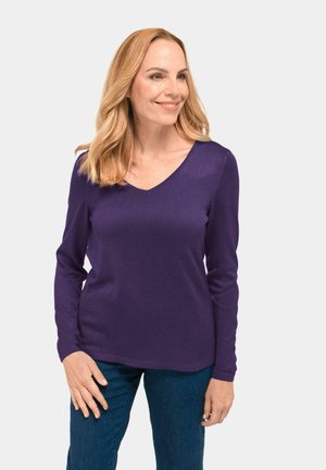 Lila langärmliger V-Ausschnitt-Pullover aus gestricktem Stoff. Glatte Textur, lässige Passform, getragen mit blauen Jeans. Keine Muster oder Verzierungen.