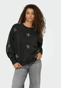 Maglione nero con decorazioni a forma di stella, maniche lunghe e una vestibilità comoda. Presenta un collo rotondo e dettagli di cuciture a vista.