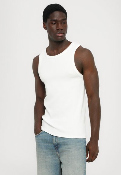 Débardeur en coton blanc avec un col arrondi et de larges bretelles, associé à un jean en denim bleu clair. Texture lisse et coupe ajustée.