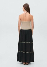 Maxi dress with a beige fitted top and a flowing black skirt. The skirt has decorative stitching across the seams. Soft fabric, halter tie.