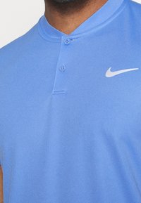 Polo azul de Nike con cuello abotonado, textura suave y un pequeño logo blanco en el pecho.