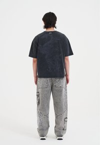 Mørkegrå oversized t-shirt med en dragegrafik på ryggen, parret med lysegrå cargo-bukser med hvid broderi og patches.