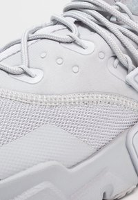 Ljusgrå sneakers med ovandel i mesh, släta detaljer, ton-i-ton-sömmar och texturerad gummisula. Skosnörena är tätt åtdragna med plastöglor.