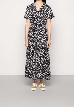 Maxi dress in navy fabric with white floral print, short sleeves, and a v-neck. Features a fitted waist and lightly pleated skirt. Paired with tan sneakers.