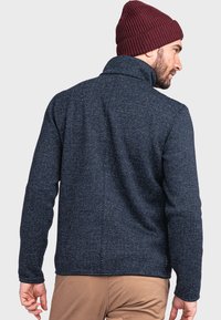 Marineblaue Fleecejacke mit einem strukturierten Muster, hohem Kragen und langen Ärmeln. Kombiniert mit einer bordeauxroten Strickmütze.