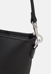 Črna usnjena torba z teksturirano površino, z adornirano srebrno zaponko in nastavljivim trakom. Oblikovanje je minimalisticno in funkcionalno.