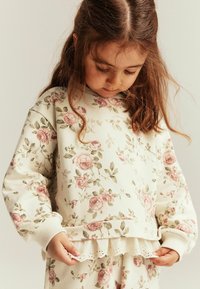 Kukkapainatuksellinen, kermavärinen collegepaita, jossa on pitkät hihat, ryhmätyypin hihansuut ja koristeellinen pitsireunus helmassa. Pehmeä puuvillasekoitemateriaali.