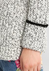 Stickad tröja i svart och vitt med ett texturerat mönster. Har en svart detalj vid manschetten och blommig broderi på den blåa denim.