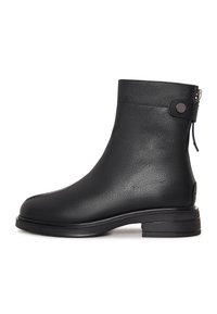 Bota de cuero negra de media caña con punta redondeada, correa decorativa y botón cerca de la parte superior, y un tacón bajo cuadrado sobre un fondo blanco.