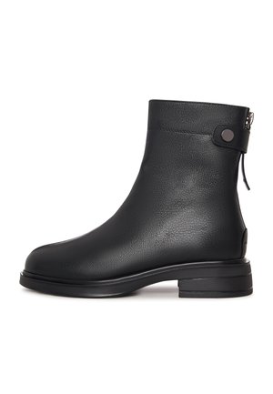 Černá kožená bota do poloviny lýtek s kulatou špičkou, dekoračním páskem a knoflíkem blízko vršku a nízkým blokovým podpatkem na bílém pozadí.