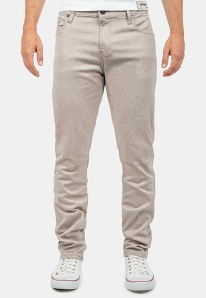 Beige Baumwollmischungshosen mit strukturiertem Gewebe, schlanker Passform, fünf Taschen-Design und schwarzem Knopfverschluss. Kombiniert mit weißen Turnschuhen.