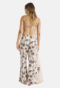 Dvojdielny outfit pozostávajúci z hnedého bandeau topu s prevedením palmových listov a smotanových nohavíc s rovnakým vzorom. Mäkka tkanina, voľný strih.