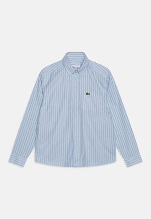 Camisa de manga larga azul claro con botones, con rayas verticales blancas y azules y un pequeño logo de cocodrilo verde en el bolsillo del pecho izquierdo.