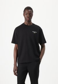 Black short-sleeve t-shirt made of cotton, featuring front embroidery reading "Jeu Set et Match" and a logo detail. Simple, relaxed cut.