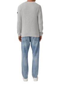Grauer gerippter Strickpullover mit langen Ärmeln, kombiniert mit hellblauen lockeren Jeans und weißen Sneakers, von hinten gesehen.