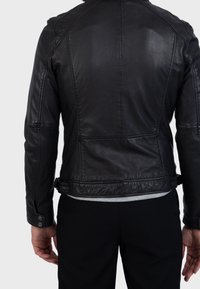 Musta nahkatakki, jossa on hieman teksturoitu pinta ja näkyvät ompeleet. Ominaisuuksiin kuuluu kapeahko istuvuus, napilliset hihansuut ja helmassa säädettävä metalliosio.