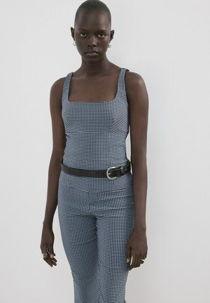 Črnec, oblečen v modro-belo karo brezrokavnik in ujemajoče hlače, dopolnjene s črnim pasom in srebrnimi obročastimi uhančki.