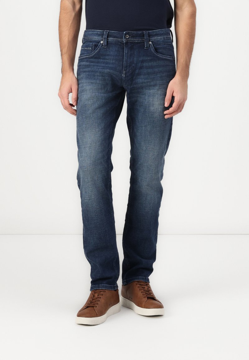 Jeans in denim blu scuro a sigaretta, con una leggera sfumatura, cinque tasche e chiusura classica con bottone. Abbinate a sneakers marroni con lacci.