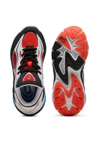 Un par de zapatillas deportivas en rojo, blanco y negro; el zapato izquierdo muestra la parte superior con los cordones, el zapato derecho muestra la suela con la marca RS y patrones de agarre.