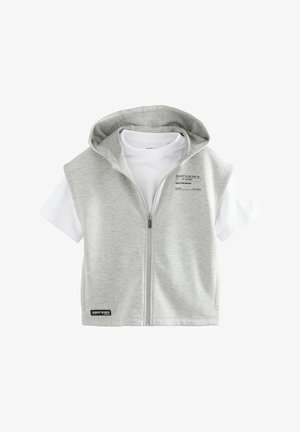 Lichtgrijze ritssluiting vest met capuchon over een wit T-shirt. Kenmerkt zich door een bedrukte label op het vest en een zwart accentlabel aan de onderkant.
