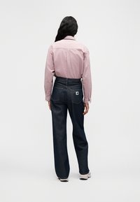 Κόκκινο πουκάμισο με μακριά μανίκια και καρό μοτίβο, καθώς και σκούρο μπλε τζιν παντελόνι με φαρδιά μπατζάκια και υφή. Το τζιν έχει λεπτομέρεια ετικέτας στην πίσω τσέπη.