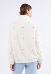 Polarowy kurtka, w kolorze kremowym z niebieskimi haftowanymi detalami. Posiada wysoki kołnierz i elastyczny pas. Miękka, teksturowana powierzchnia.