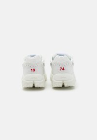 White athletic shoes featuring a textured sole, padded collar, and pronounced heel. Red numbers 19 and 74 are visible on the back.