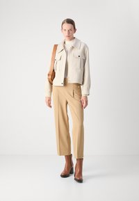 Creme farvet cropped jakke med to forlommer, beige bukser og brune blokhælede ankelstøvler. Glat tekstur og skræddersyet pasform.