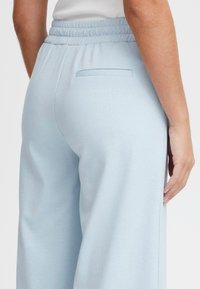 Lichtblauwe, hooggehakte broek van zachte stof. Heeft een elastische tailleband en een achterzak. Rechte pijpen met minimale textuur.