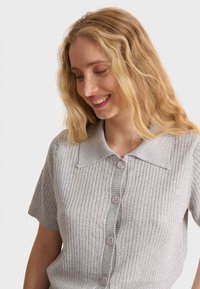 Short-sleeve, collared sweater in light gray ribbed fabric with subtle shimmer, featuring four large buttons down the front.