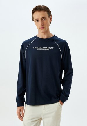 Marineblå langærmet t-shirt lavet af bomuld, med hvid tekst i atletisk tema og kontrastfarvet piping langs raglanærmerne.