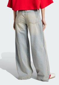 Light blue wide-leg jeans with a faded finish, featuring rear pockets and a clean design. Worn with a loose red shirt and white shoes.