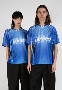Modré futbalové dresy s krátkym rukávom a gradientným dizajnom. Biele nápisy "wasted", čierne akcenty a logo na hrudi. Čierne nohavice.