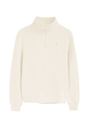 Jersey de color crema con mangas largas, cuello alto y cremallera corta en el centro delantero, con un sutil logo bordado en el pecho.