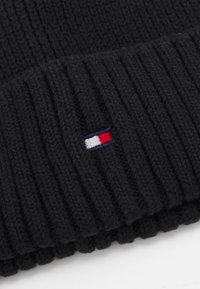 Knit black beanie with ribbed texture. Features a small embroidered logo in red, white, and blue positioned on the front.