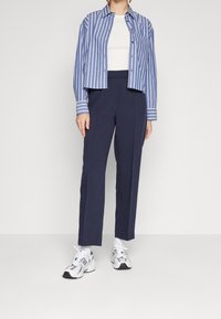 Camisa de botones a rayas azul y blanca, camiseta blanca de tirantes, pantalones tapered marinos y zapatillas blancas con acentos negros. Ajuste moderno y entallado.