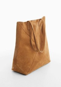 Sac fourre-tout en suède beige avec deux anses, présentant un design géométrique et des accents cousus, ainsi qu'une forme spacieuse et structurée.